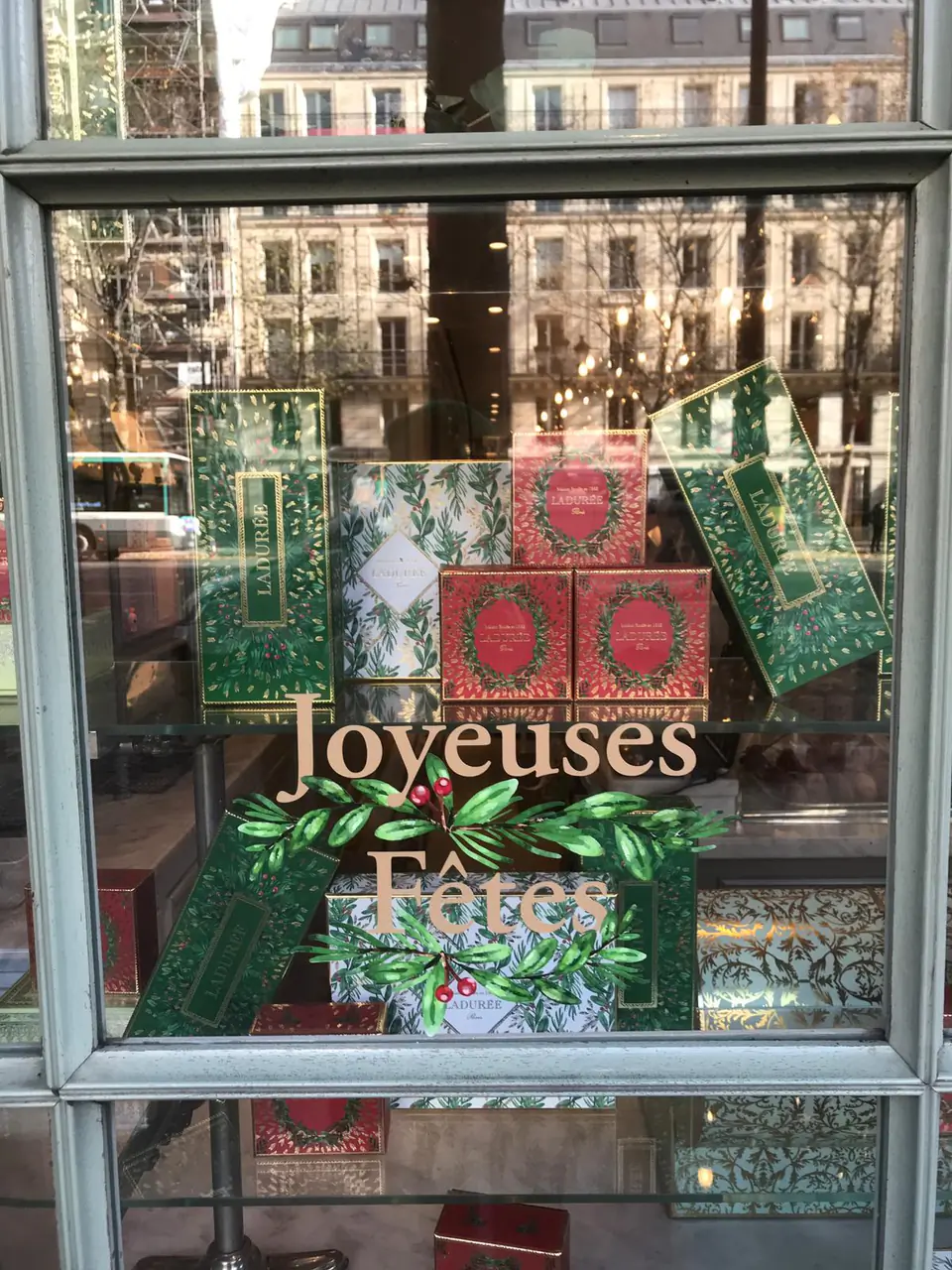 Lettrage « Joyeuses Fêtes » doré et branches de feuillage en vitrophanie sur une vitrine Ladurée