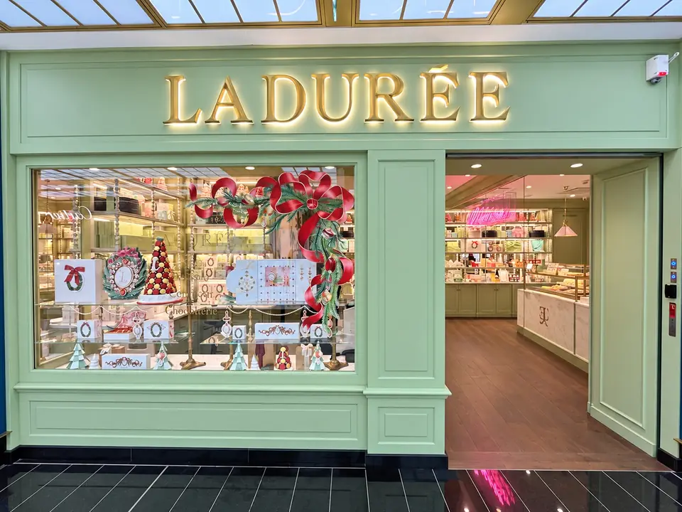 Façade Ladurée vert pâle pendant les fêtes : vitrine de Noël avec couronnes de ruban rouge et décor en vitrophanie.