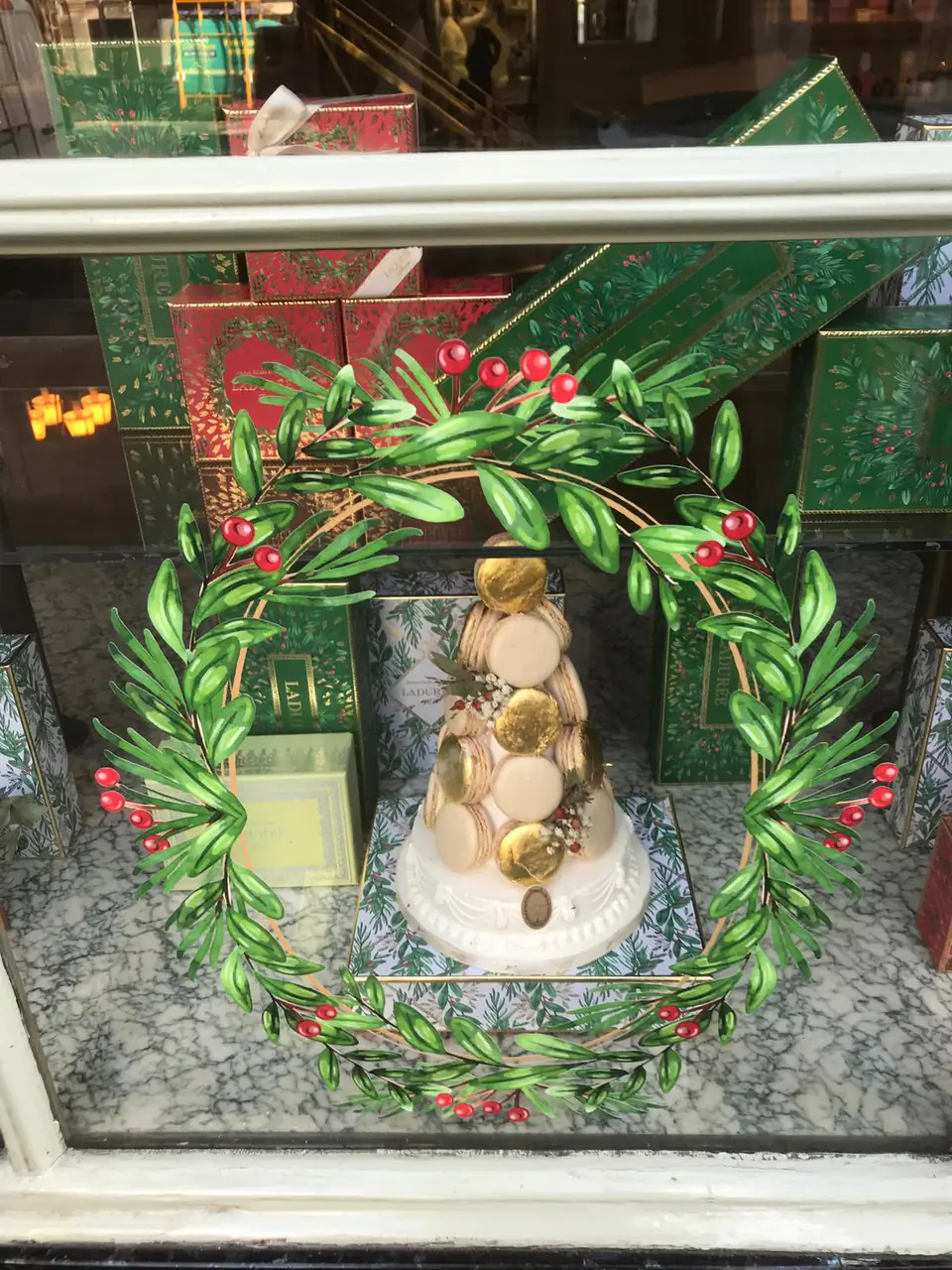 Lettrage « Joyeuses Fêtes » et feuillage en vitrophanie devant des coffrets de Noël Ladurée