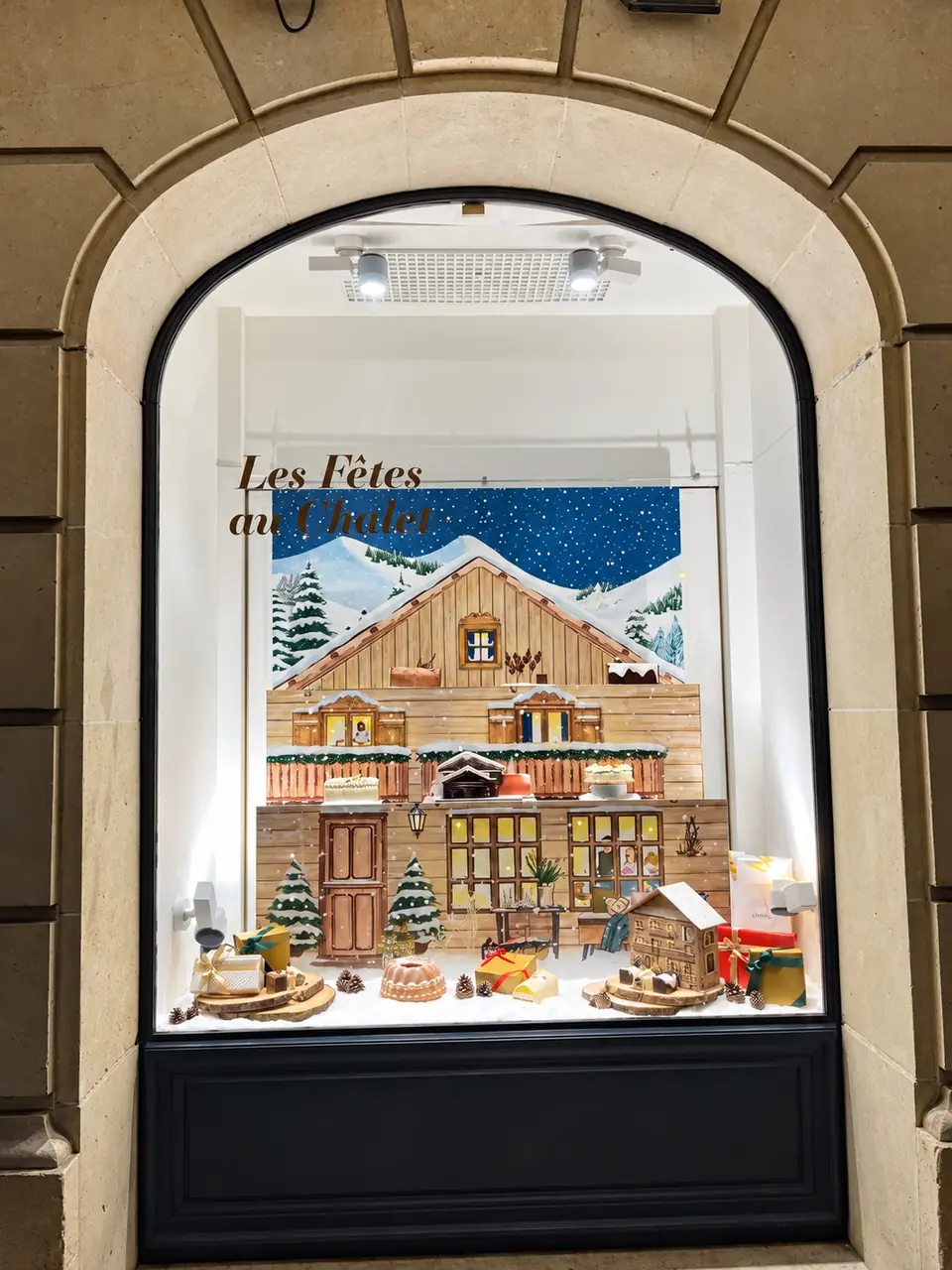 Vitrine voûtée Lenôtre « Les Fêtes au Chalet » : chalet enneigé, ciel étoilé et lettrage en vitrophanie.