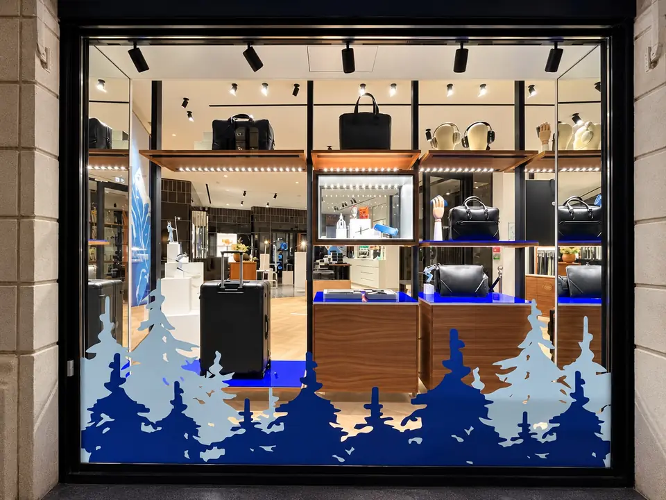 Vitrine Montblanc de nuit : forêt de sapins graphiques bleus en vitrophanie en partie basse, boutique éclairée.
