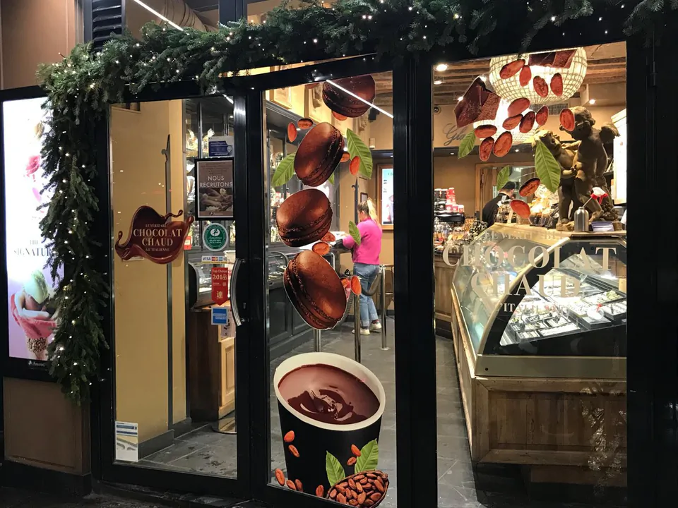 Vitrophanie d'hiver Amorino : macarons au chocolat et tasse de chocolat chaud imprimés sur la porte vitrée, guirlande de sapin